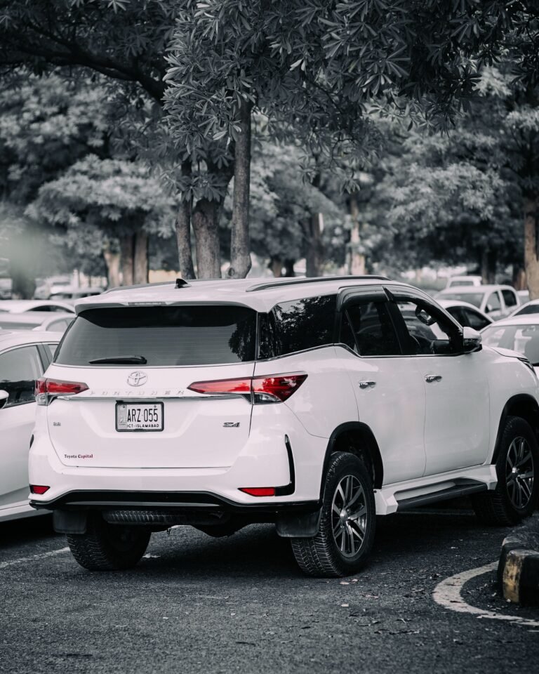 White SUV parked in a tree-lined outdoor parking lot on a clear day.